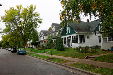 A look down a residential street with houses, sidewalk and cars.