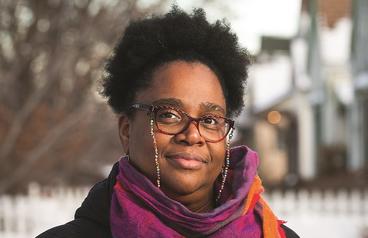 Outdoor headshot of Taiyon J. Coleman wearing glasses and a magenta scarf.
