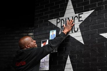 A black man with a tear in his eye touching the Prince star on First Avenue's wall after Prince's death.