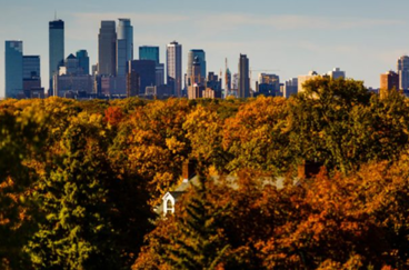 An aerial view of a spire at St. Thomas University in the fall and you can also see the Mpls skyline behind it 
