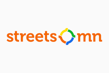 orange text "streets mn" with an icon in between the two words that is in 4 primary colors and looks like a roundabout.
