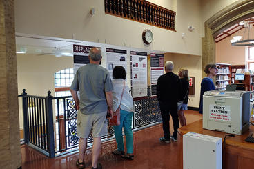 Several people standing in a public library looking at an exhibit about Displacement