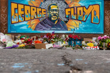 A George Floyd mural with flowers and "I can't breathe" signs on the ground in front of it.