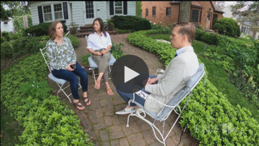 An interviewer speaks with a couple in front of their house